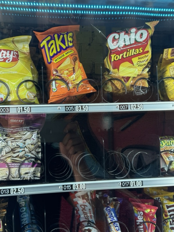 Chipstüten von Lay's, Takis und Chio hinter Glas, darunter Süßigkeiten