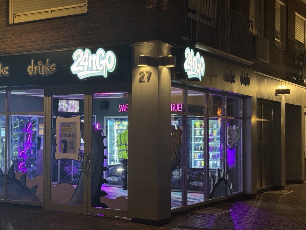 Derselbe Store bei Nacht, die Automaten leuchten durch die Schaufenster auf die Straße