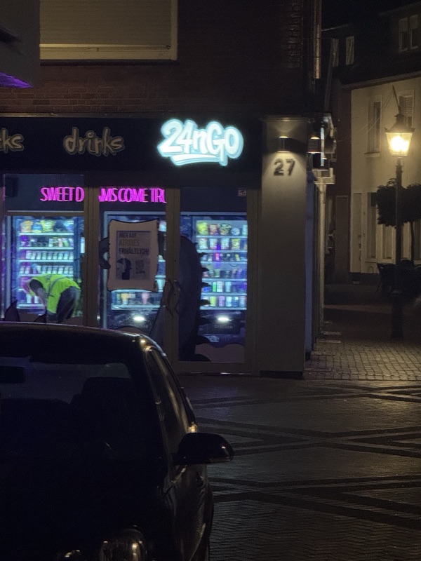 Leuchtschrift drinks und 24nGo über den Schaufenstern, davor ein parkendes Auto